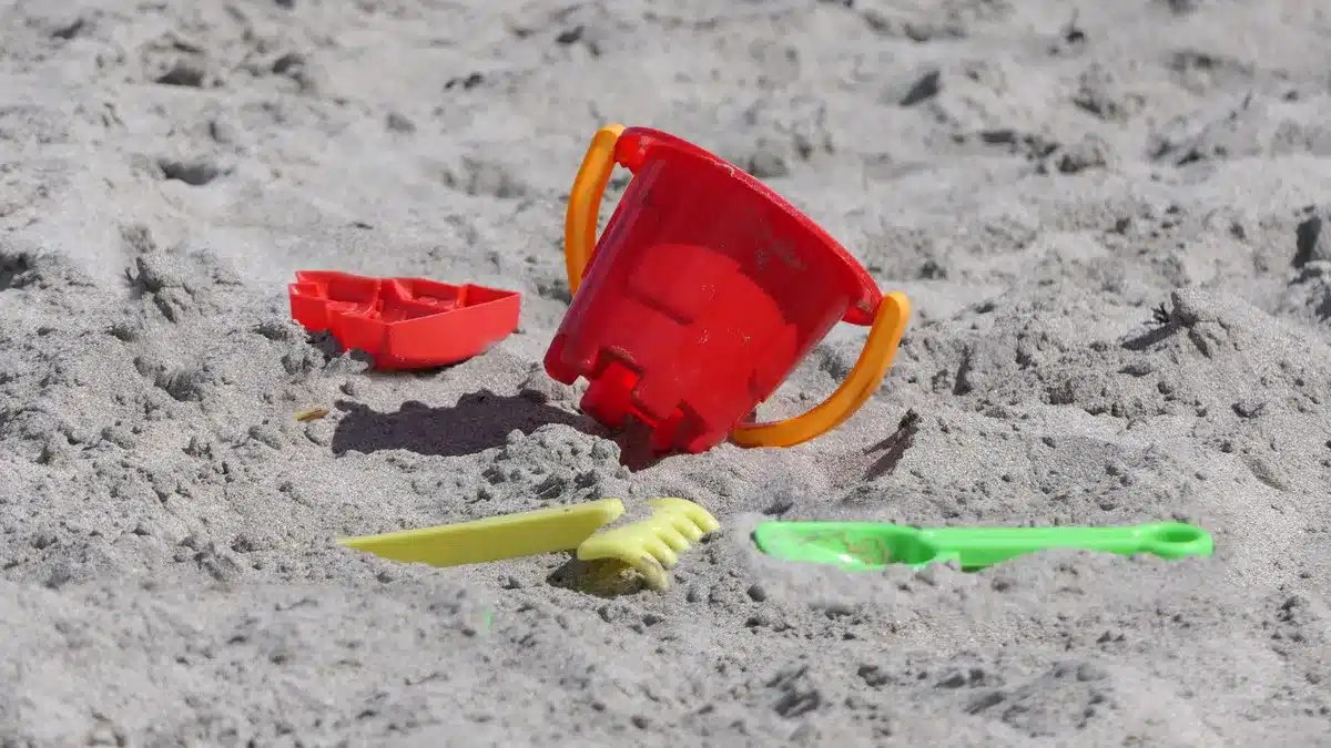 Enfant jouant avec un seau et une pelle dans le sable humide à la plage