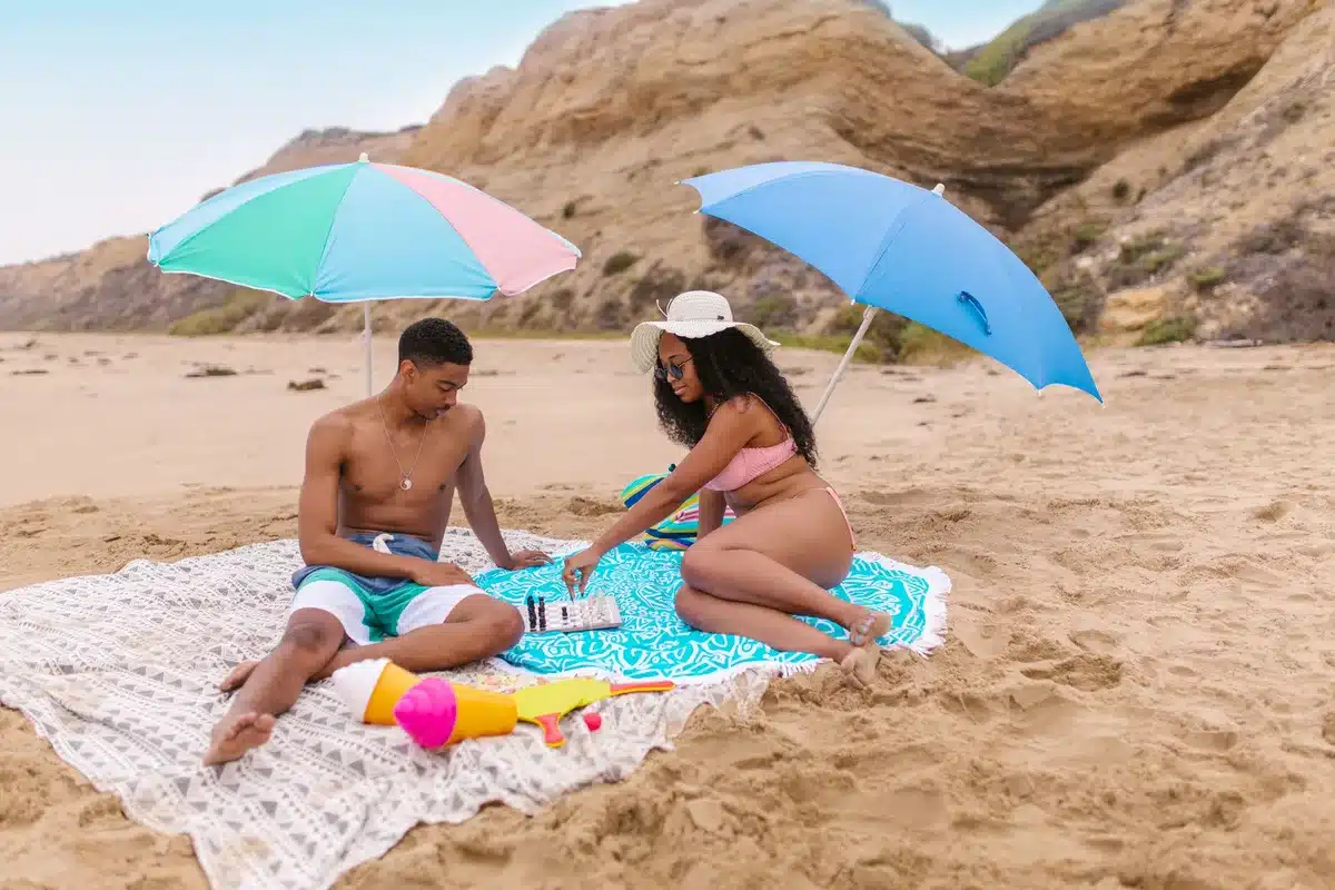 Famille pique-niquant sous un parasol à la plage avec des en-cas et une gourde