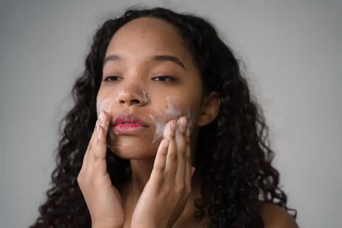 Personne effectuant un nettoyage doux du visage avec un produit léger, mains et visage en gros plan.