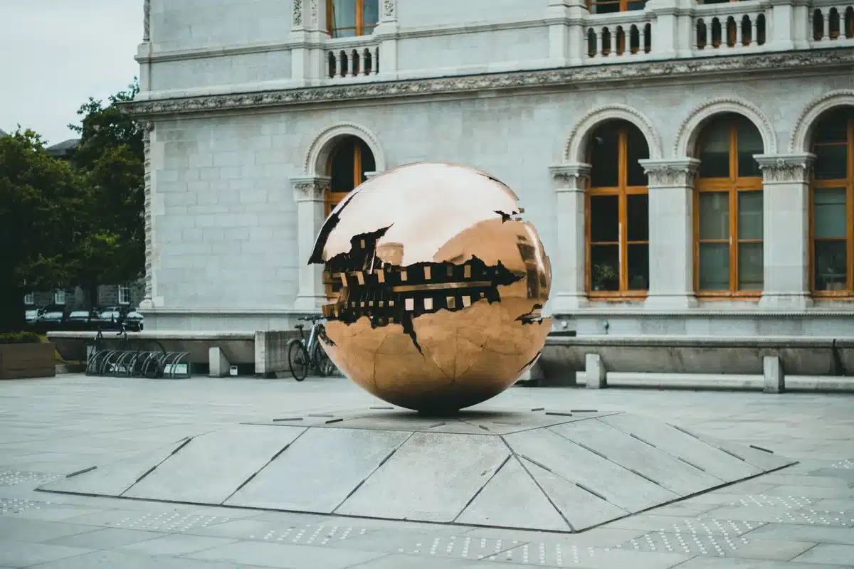 Sculpture d'art public en acier poli reflétant l'architecture environnante dans une place urbaine