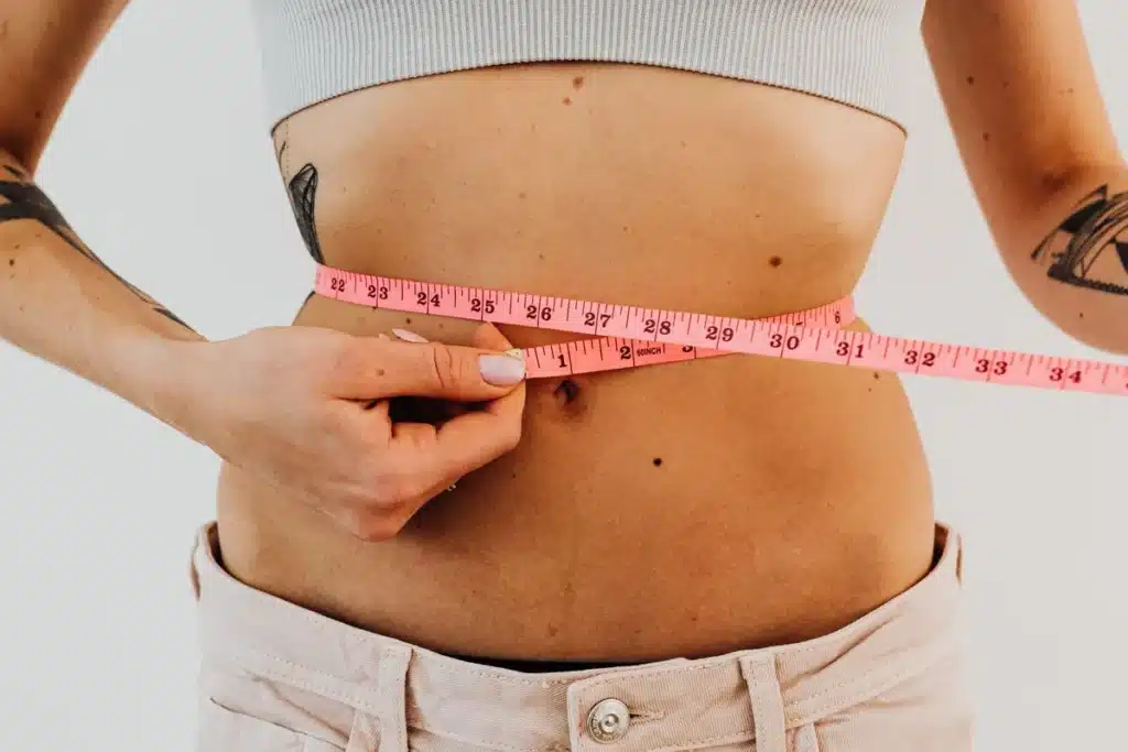 Silhouette d'une personne mesurant son tour de taille avec les mains, entourée d'objets de bien-être