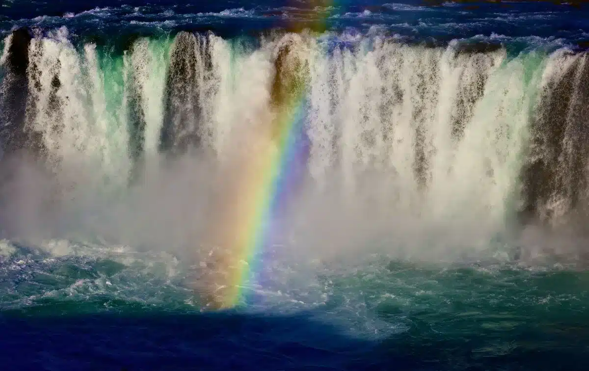 Cascade puissante entourée de roches mouillées avec un arc-en-ciel dans la bruine.
