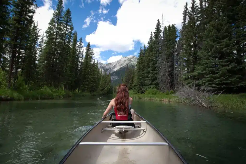 Canot solitaire sur un lac de montagne entouré de pics enneigés et de forêts de conifères.