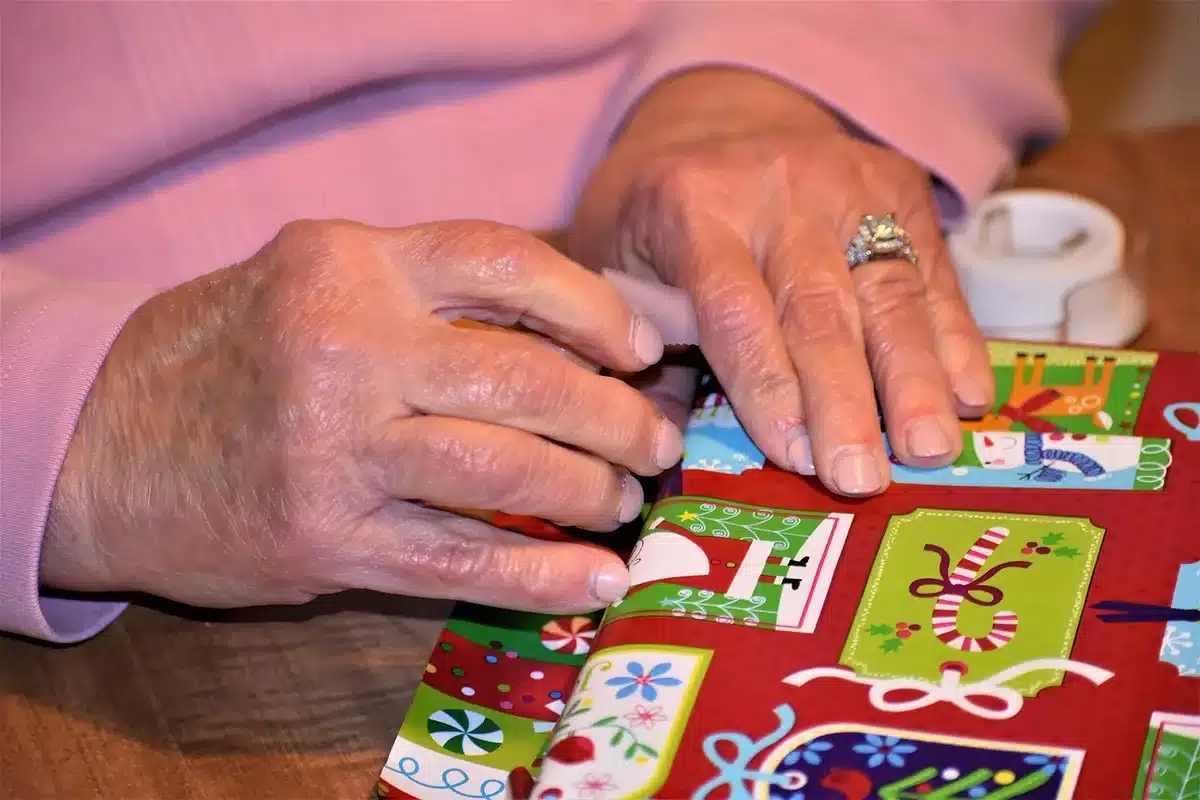 Mains emballant un cadeau de naissance dans du tissu réutilisable, entouré de jouets en bois et de livres