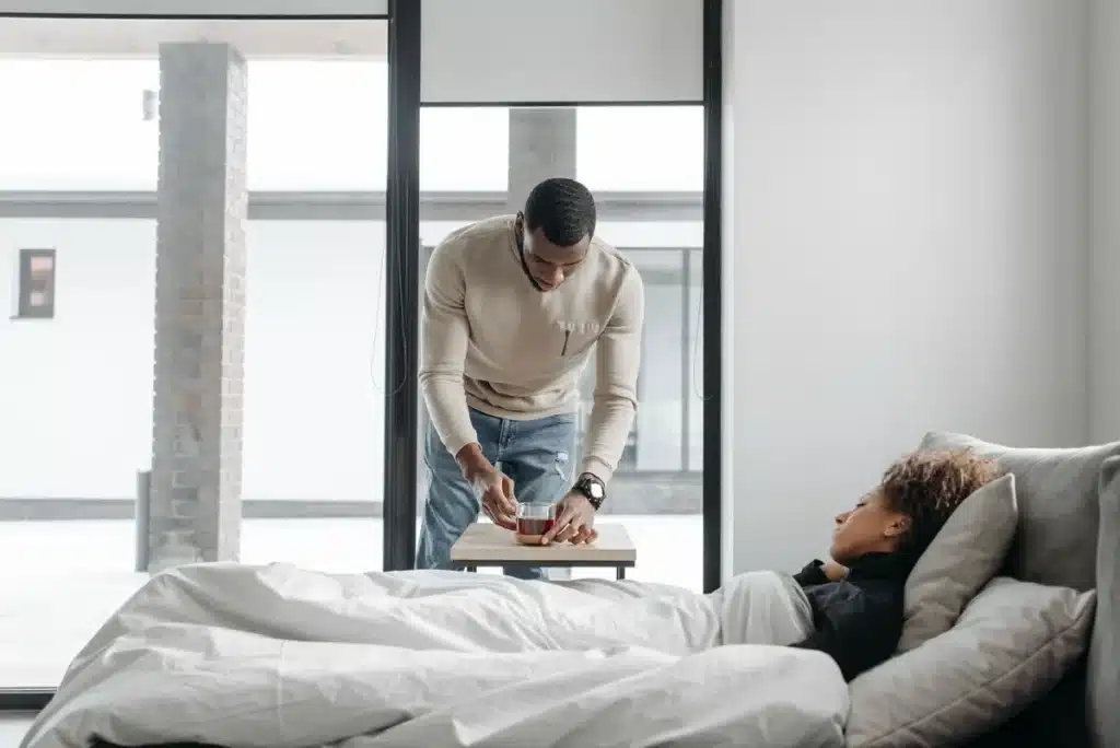 Personne se levant lentement du lit, main appuyée sur le meuble, expression de léger vertige.